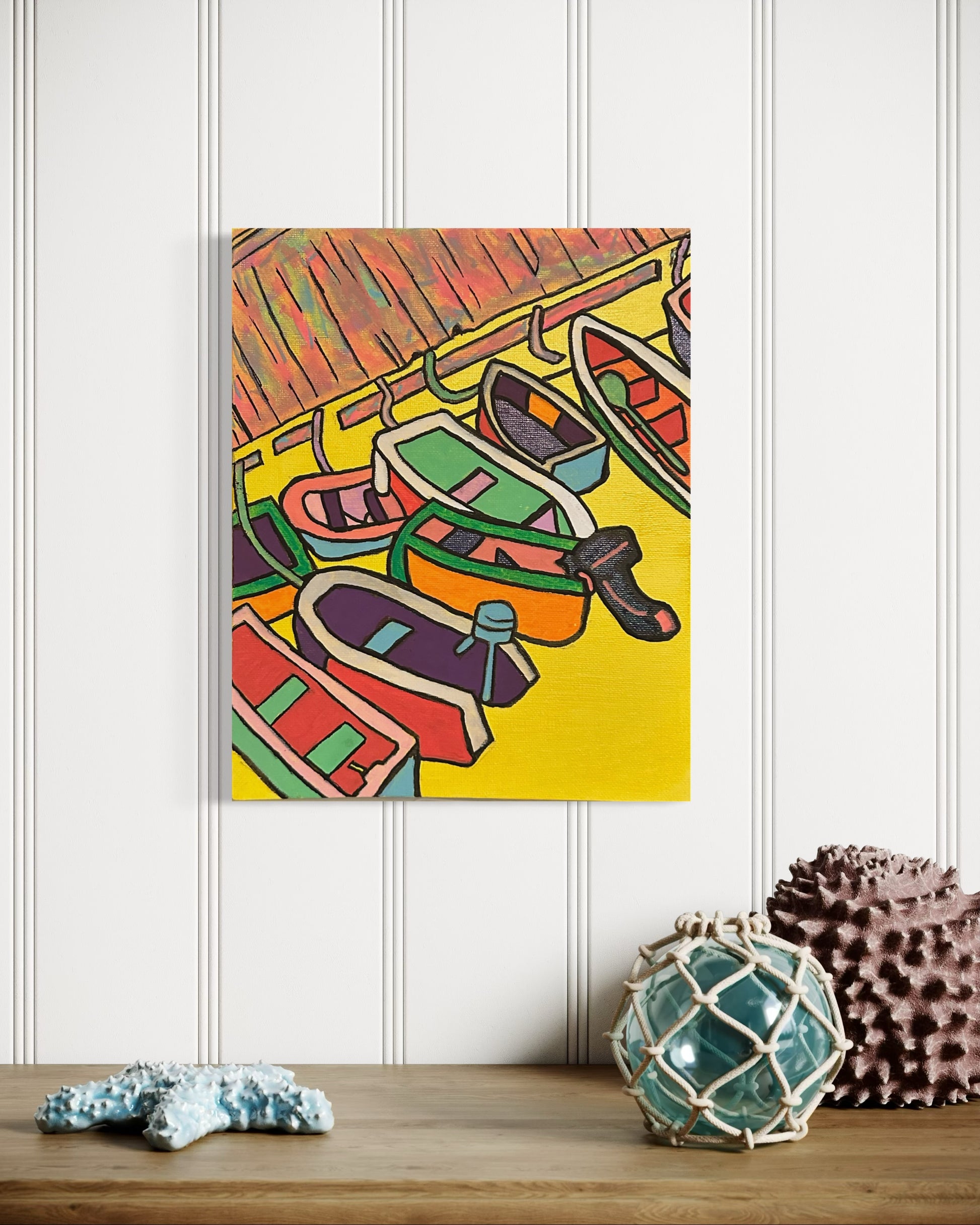 “Harbor” by Andrew French displayed above a coastal-inspired table with seashell and nautical décor, highlighting its bold yellow tones and boat details.