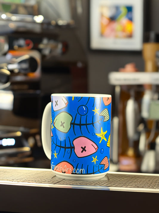 A bold ceramic mug featuring Andrew French’s vibrant “Toxic Blue Xmas Fish” design. The artwork displays whimsical fish bones, seashells, and starfish in bright holiday colors against a deep ocean-blue background — a playful fusion of coastal art and festive cheer.
